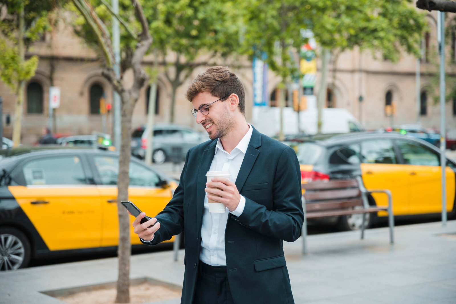 young-businessman-holding-coffee-cup-looking-mobile-phone